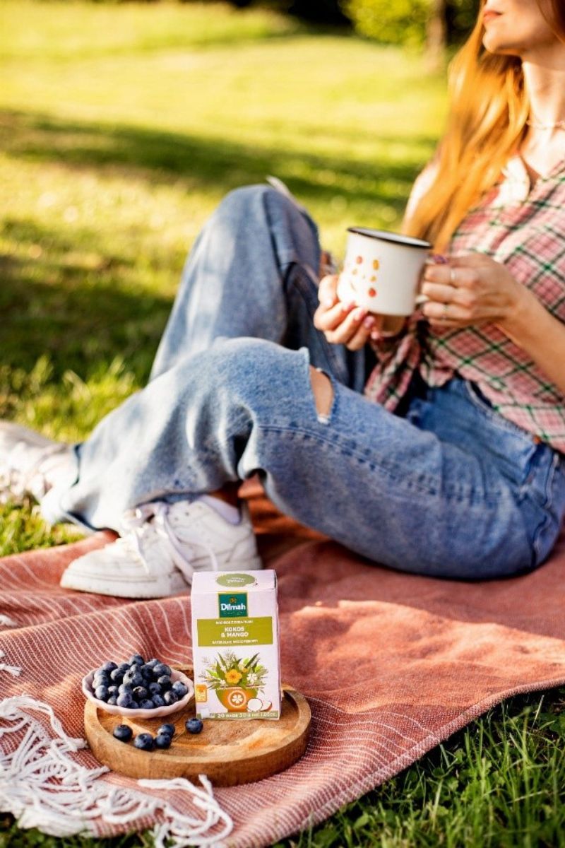 Kobieta relaksująca się podczas pikniku, pijąc roiboss Dilmah na zimno.