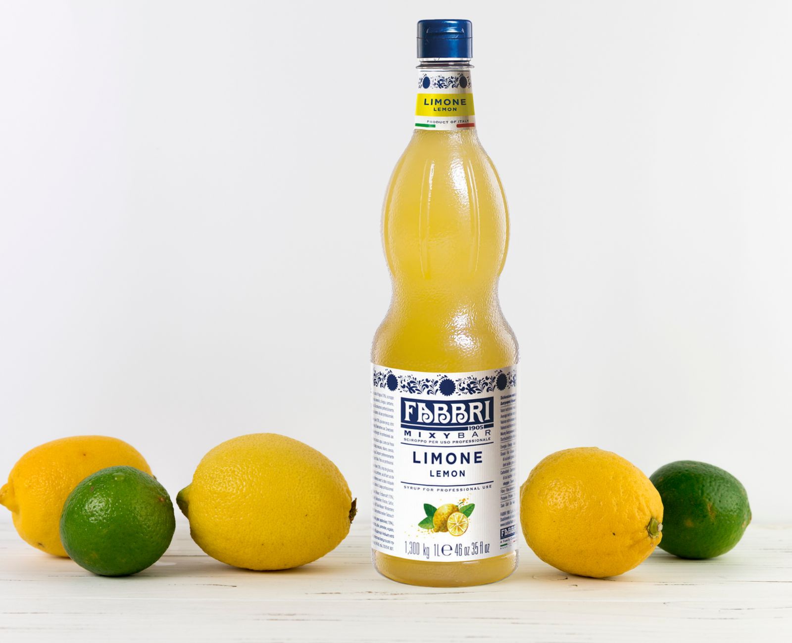 Włoski syrop cytrynowy Fabbri Mixybar Limone do lemoniady i koktajli, ustawiony na blacie wśród świeżych cytryn i limonek, w jasnym, naturalnym świetle.