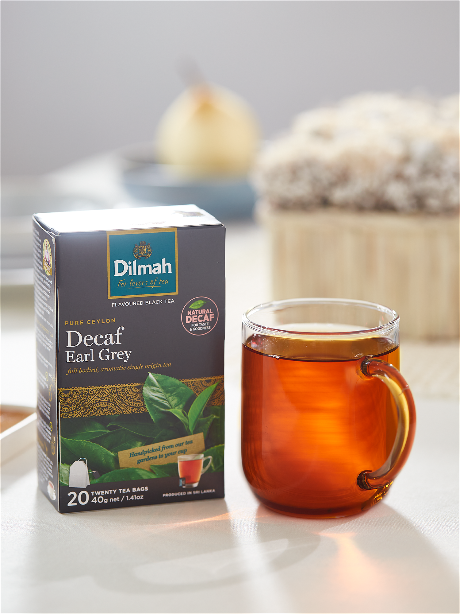 Bezkofeinowa herbata Dilmah Decaf Earl Grey w szklanym kubku na kuchennym blacie. Obok opakowanie produktu.
