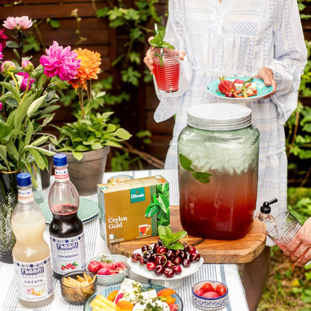 Herbata Dilmah z lemoniadą na bazie syropów Fabbri podawana podczas garden party. Na stole owoce, przekąski, słoik z lemoniadą herbacianą i dwa syropy do lemoniad Fabbri.