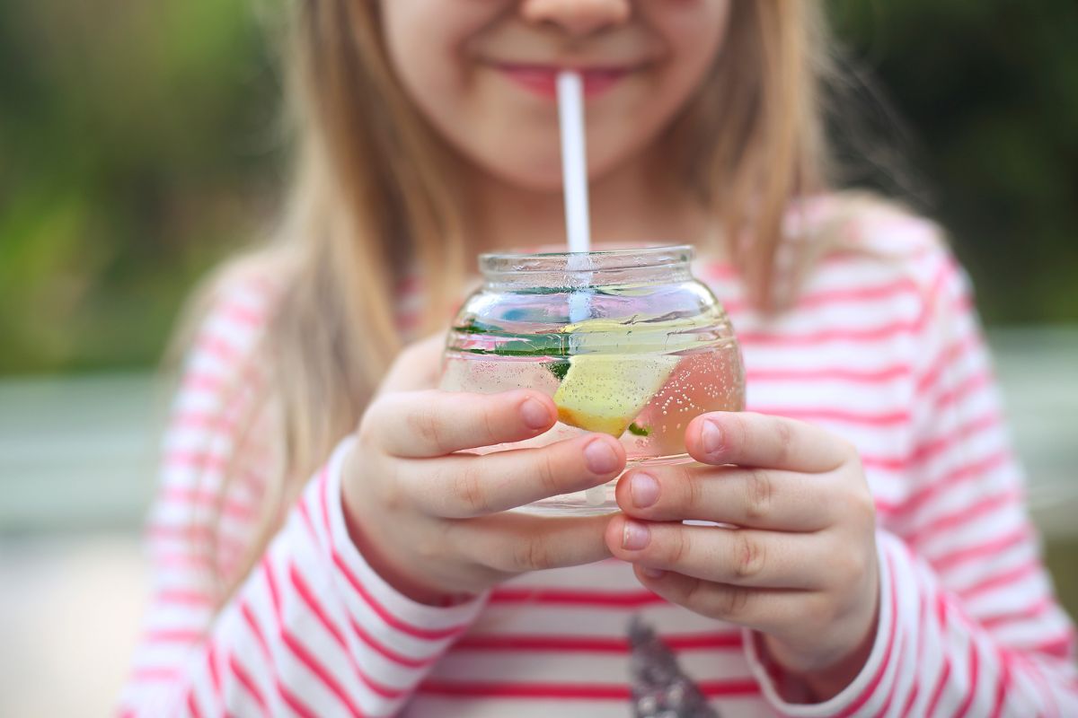 Mała dziewczynka pije lemoniadę ananasową w słoneczny dzień.