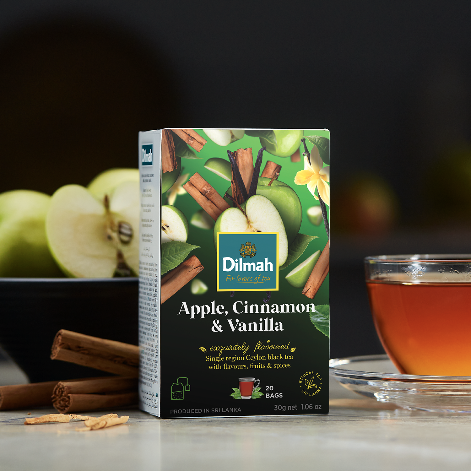 Herbata jabłkowo-cynamonowa Dilmah Apple, Cinnamon & Vanilla w towarzystwie jabłek i lasek cynamonu.