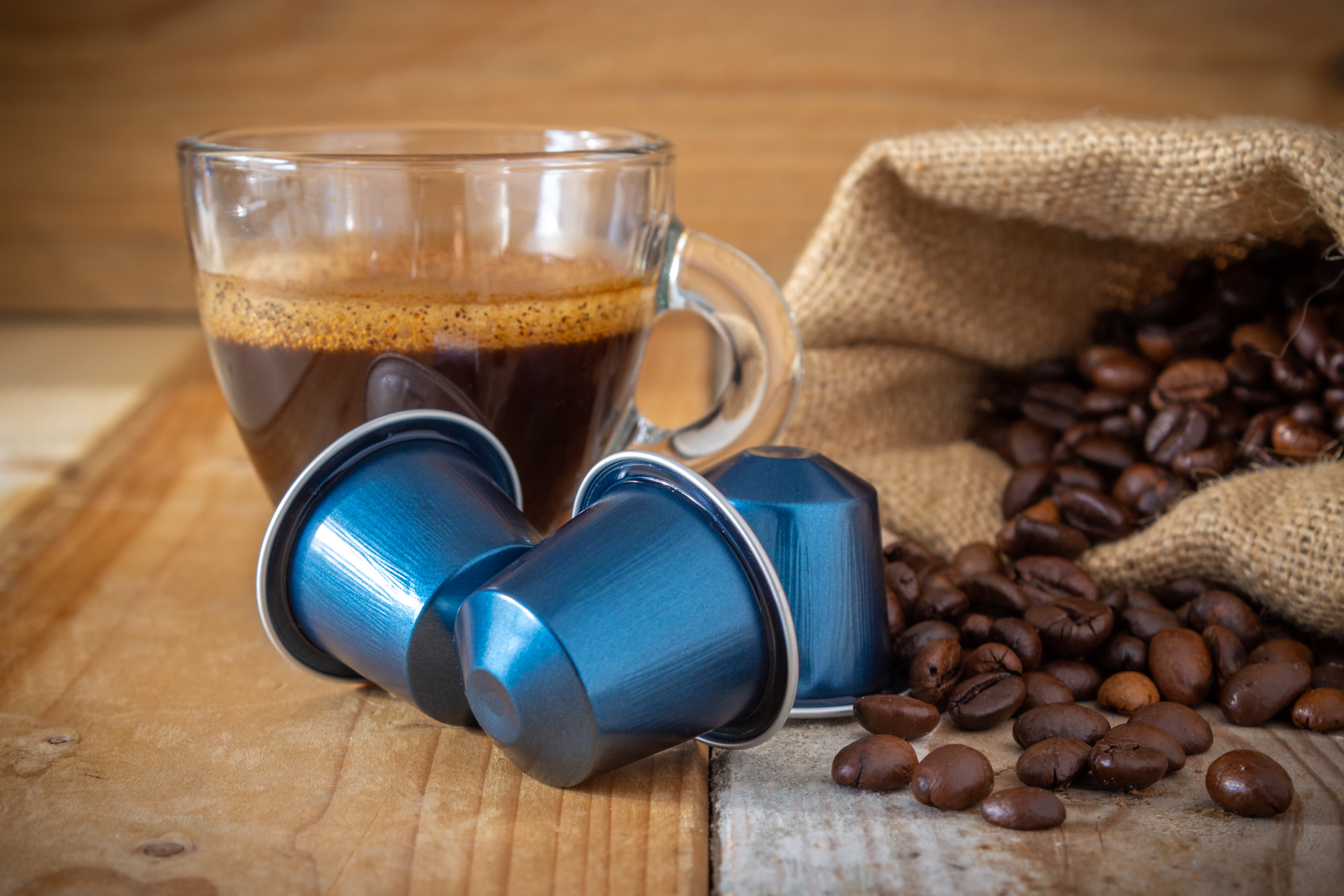 Kapsułki z kawą Saquella Decaf Espresso Aromatico obok kubka z kawą i rozsypanych ziaren kawowych – zestawienie prezentujące bezkofeinową kawę włoskiej marki Saquella, idealną do ekspresów kapsułkowych Nespresso.