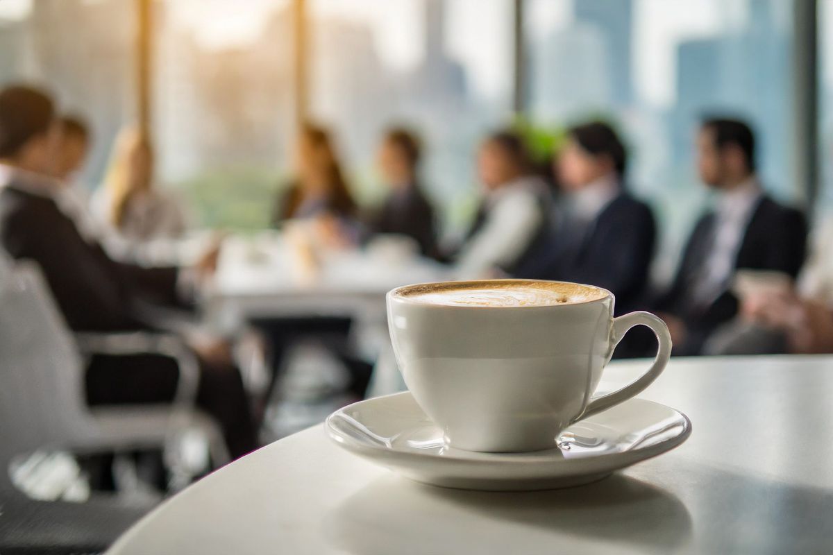 Filiżanka kawy Saquella stojąca na stole, w tle widoczni uczestnicy konferencji podczas spotkania.